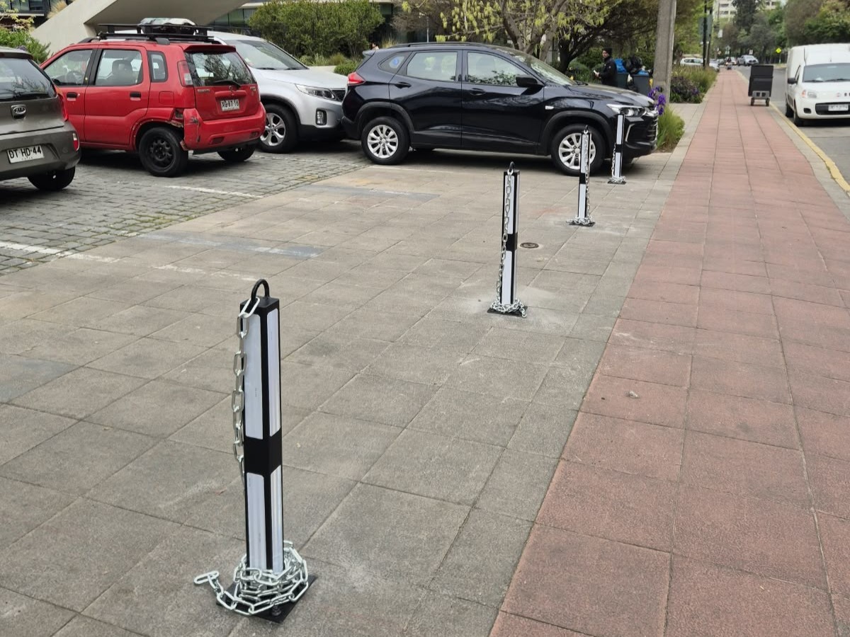 Pilona fija negra con cintas reflectantes y cadena recogida en su base